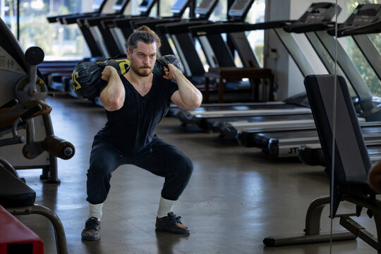 Caucasian muscular body builder sport man is practice weight training on sandbag lunges for core muscle inside gym for exercising and hyrox workout concept