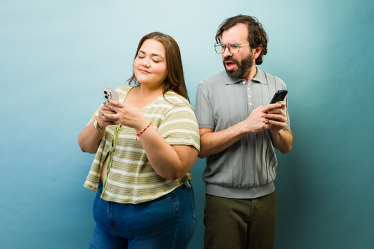 Cheating girlfriend texting on her smartphone, while her boyfriend is trying to spy on her messages and social media