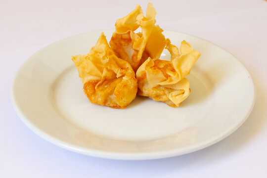 Crispy fried wontons or pangsit goreng served on white ceramic plate. Asian appetizer, Chinese snack and street food concept.