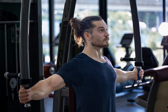 Caucasian man with strong and muscular body training on chest press machine in gym for muscle building and weight lifting practice with back light
