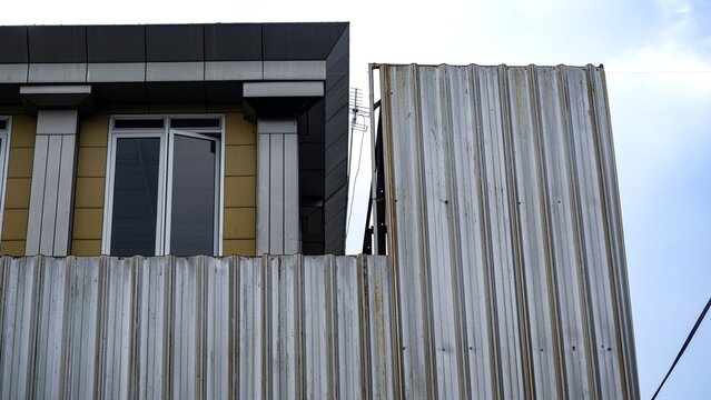The exterior of a commercial building featuring a blend of corrugated zinc cladding and modern wall panels, serving as weather and security protection for the structure during renovation.