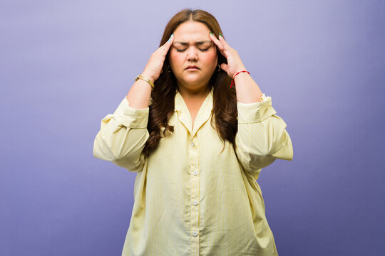 Overweight woman experiencing intense pain and discomfort, holding her head from stress or a strong headache