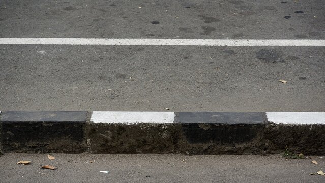 Alternating black and white painted safety curb along a city road, providing clear visual boundary marking between asphalt surfaces.