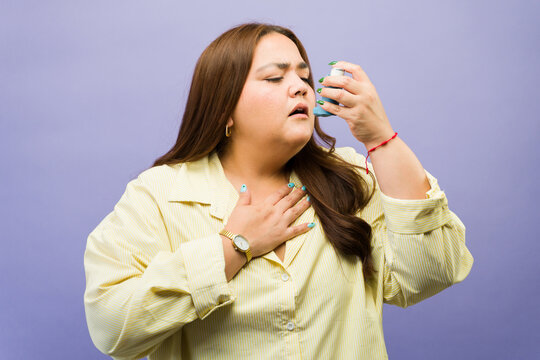 Plus size woman experiencing asthma attack, using inhaler for respiratory relief, managing difficult breathing and allergy symptoms
