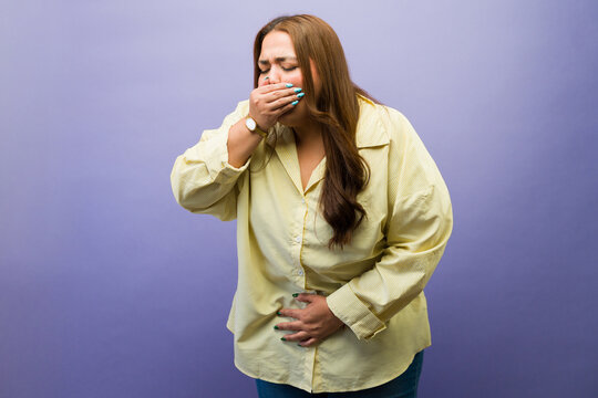 Woman feeling nauseous and unwell, covering mouth and holding stomach due to sickness or indigestion