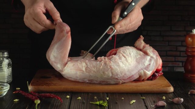 A chef in a black apron continues to inspect a large piece of raw meat on a wooden cutting board, surrounded by spices, garlic and kitchen utensils in a rustic kitchen environment