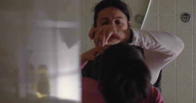Mother brushes young child&rsquo;s teeth during nightly bathroom routine at home, managing daily caregiving demands with patience, consistency and devoted modern parenting