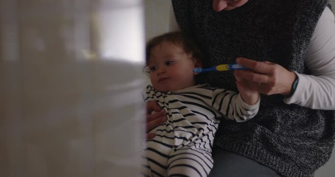 Mother brushes toddler&rsquo;s teeth while holding him during nightly bathroom routine at home, balancing hygiene, patience, childcare and devoted modern motherhood