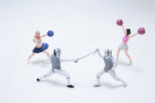 Miniature cheerleaders cheering two fencing athletes