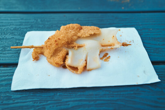 Fried squid on a wooden skewer on a blue picnic table