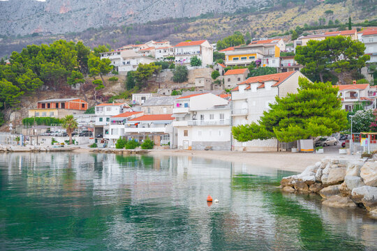 Scenic village with white houses and orange roofs on the Adriatic coast at the base of a rocky mountain in Croatia.