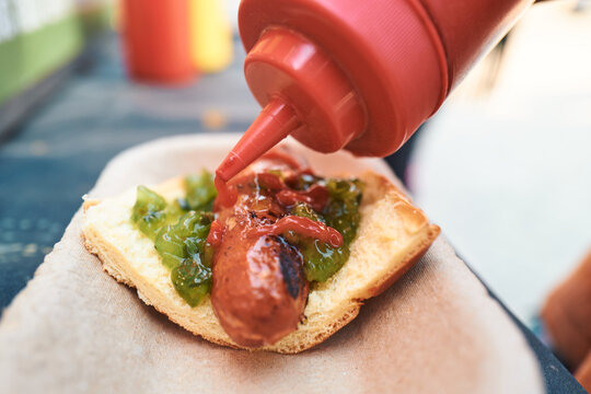 Ketchup being squeezed from a red bottle onto a loaded hot dog