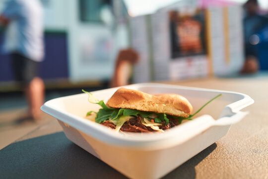 Pulled pork sandwich with a food truck behind at a festival