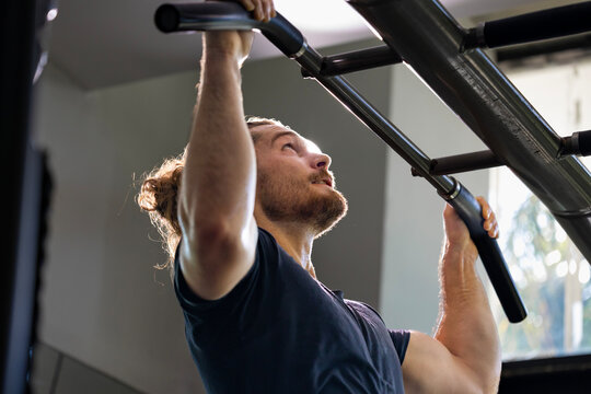Portrait of caucasian muscular sport man using hanging bar inside gym with dark background for exercise and workout in high contrast low key lighting studio
