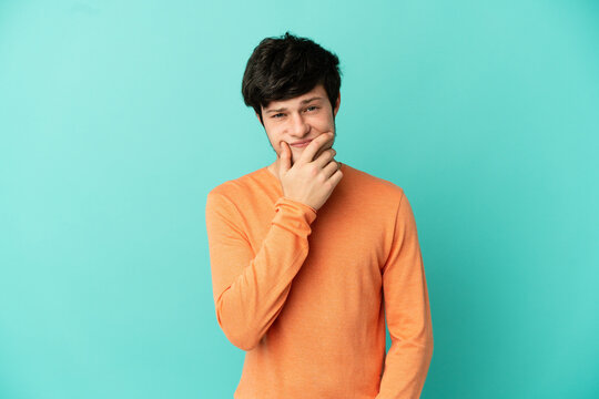 Young Russian man isolated on blue background having doubts