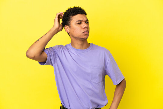 Young African American man isolated on yellow background having doubts while scratching head