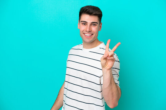 Young caucasian man isolated on blue background smiling and showing victory sign