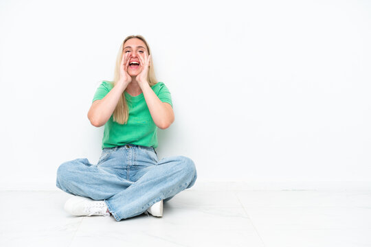 Young caucasian woman sitting on the floor isolated on white background shouting and announcing something
