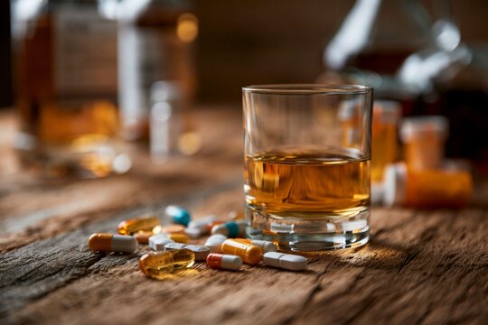 Glass of whiskey on a wooden table with scattered pills and bottles in the background