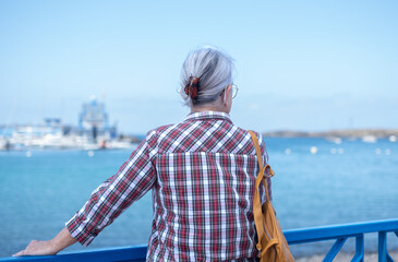 Fototapeta premium Senior adult woman enjoying seaside view from marina, contemplating retirement and peaceful travel, embracing freedom and solitude by the ocean