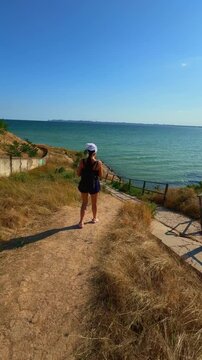 Young woman walking down a coastal path toward the sea on a sunny day back view. Ideal for Reels, TikTok, and Shorts on summer travel, active lifestyle, coastal walks, and holiday vlogs.