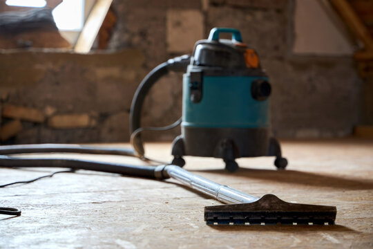 Industrial vacuum cleaner on dusty unfinished floor during house attic renovation process. Professional construction appliance prepares surface for underlayment setup.