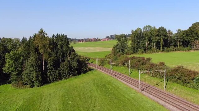 Aerial drone view of the railway line between Rotkreuz and Oberr&uuml;ti crossing the Reuss River, surrounded by green farmland and rural Swiss countryside on a sunny day.