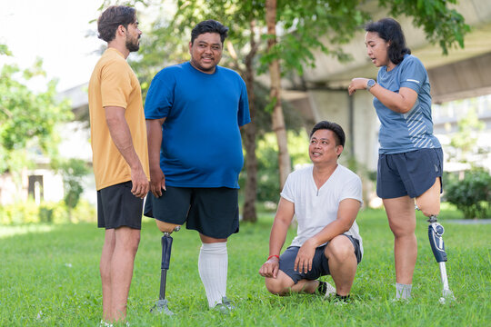 Multiethnic group of diverse people including amputee with prosthetic legs stretching arms together in public park. Inclusive diversity friends with prosthesis warming up before exercise.