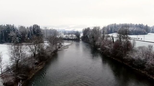 Aerial drone flight over the Reuss River near Sins, Switzerland, showing a snow covered winter landscape with railway line, river and rural countryside.