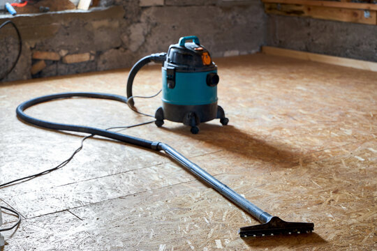 Industrial vacuum cleaner on dusty unfinished floor during house attic renovation process. Professional construction appliance prepares surface for underlayment setup.