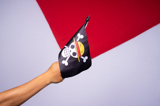 Riau, August 1, 2026, A hand holds a small flag with the Straw Hat Pirates "Jolly Roger" from the popular anime One Piece against red and white background.
