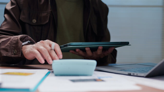 Man calculates cost reviewing corporate financial records holding tablet office desk workspace economy investment strategy planning budgeting auditing revenue analysis tax accounting ledger cash flow.