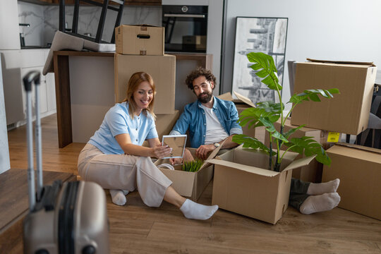 Couple relaxes on the floor surrounded by moving boxes while using a tablet in their new home