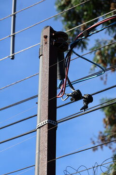 Close up of a weathered utility pole with electrical wires and insulators against a clear blue sky