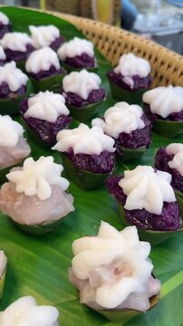 Vertical video of colorful Thai Tako desserts in banana leaf cups topped with rich coconut cream, arranged for traditional celebration.