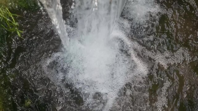Fresh spring water splashing and forming white foam with bubbles, close up top view