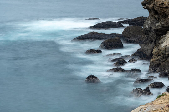 Waves crash against rocks by the shore in long exposure
