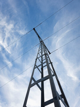 Looking up at a metal electricity pylon against a cloudy blue sky near a power line