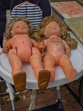 Worn retro plastic baby dolls resting together on a high chair at a flea market on a sunny day