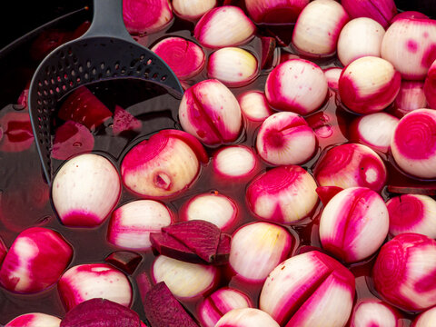 Small white onions and sliced red beets pickling in a large dark vat for food preparation