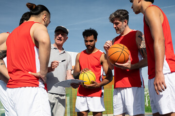 Fototapeta premium Basketball coach discussing strategy with his multi ethnic team during an outdoor practice