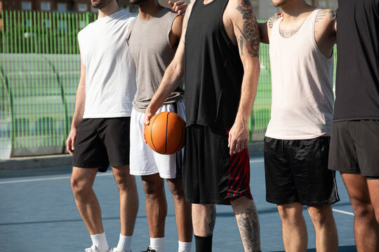 Group of diverse men standing on a basketball court, one holding a ball, symbolizing teamwork