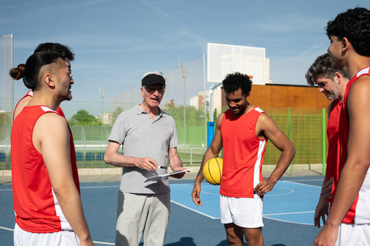 Senior coach giving instructions to a diverse group of basketball players on court