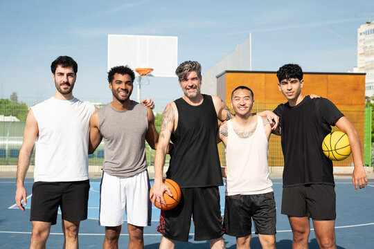Group of men standing together on a basketball court, embracing diverse team and friendship
