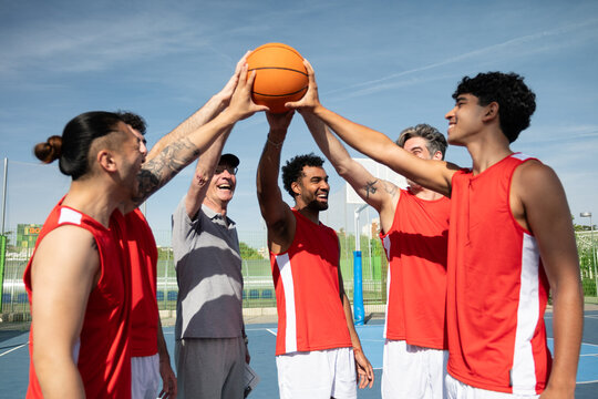 Diverse group of basketball players joining hands on a ball, symbolizing teamwork and victory
