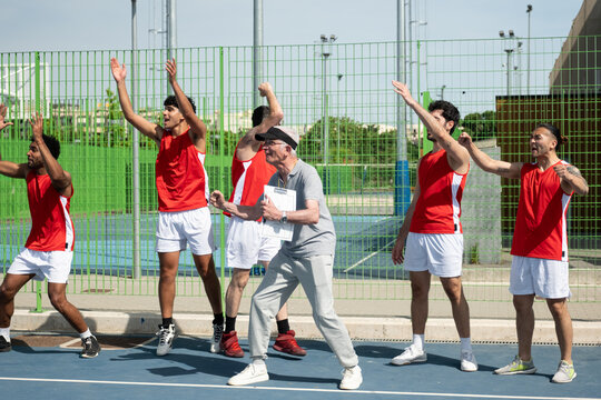 Basketball players and coach cheering during a game on an outdoor court