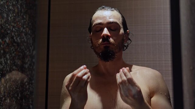 Man is washing his hair standing in the shower cabin and watching puzzled at his hands. Young adult Caucasian guy is sad because of hair loss noticed during bathing. Health and hygiene concept