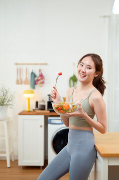 Woman Enjoys Salad in a Kitchen While Standing Near a Counter and Smiling