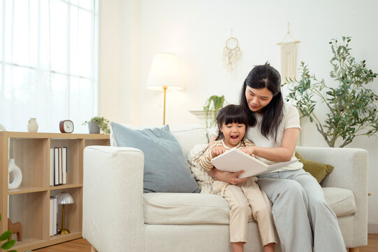 Girl Sits on a Couch While Mom Reads a Story in a Bright Living Room
