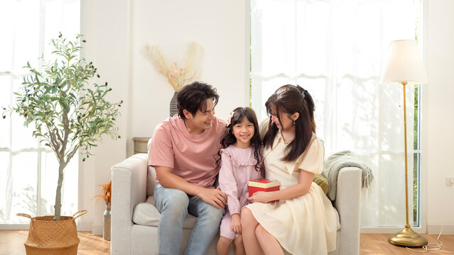 Family Sitting Together on a Couch in a Bright Room With Large Windows During the Day